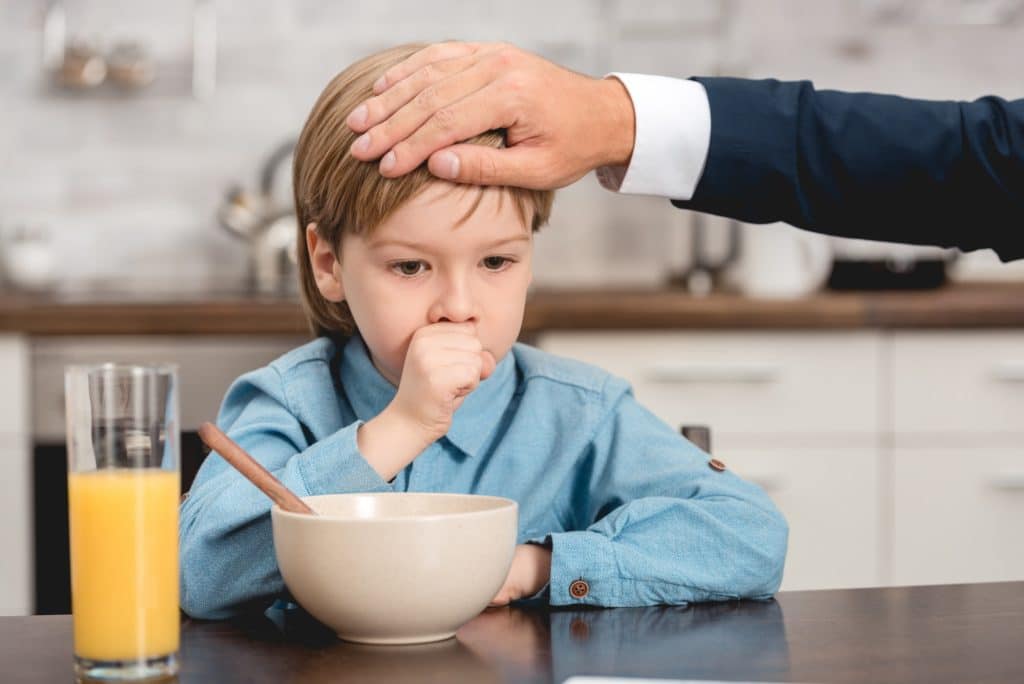 cropped shot of father checking temperature of son with hand during breakfast
