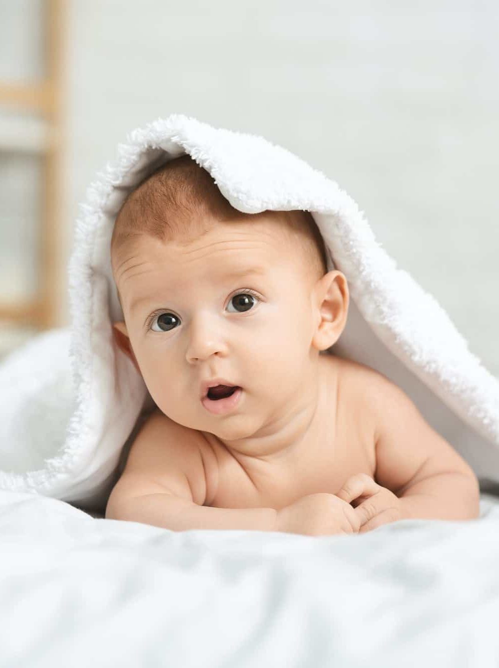 Cute newborn boy peeking out under soft white blanket