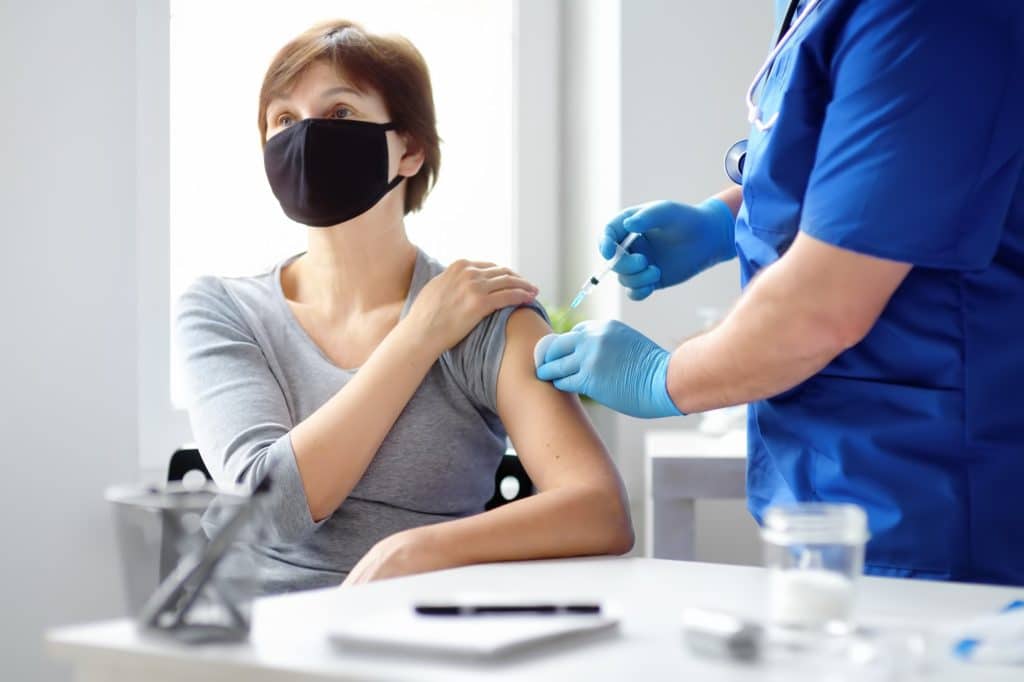 Doctor giving a mature caucasian woman a coronavirus vaccine. Mass vaccination