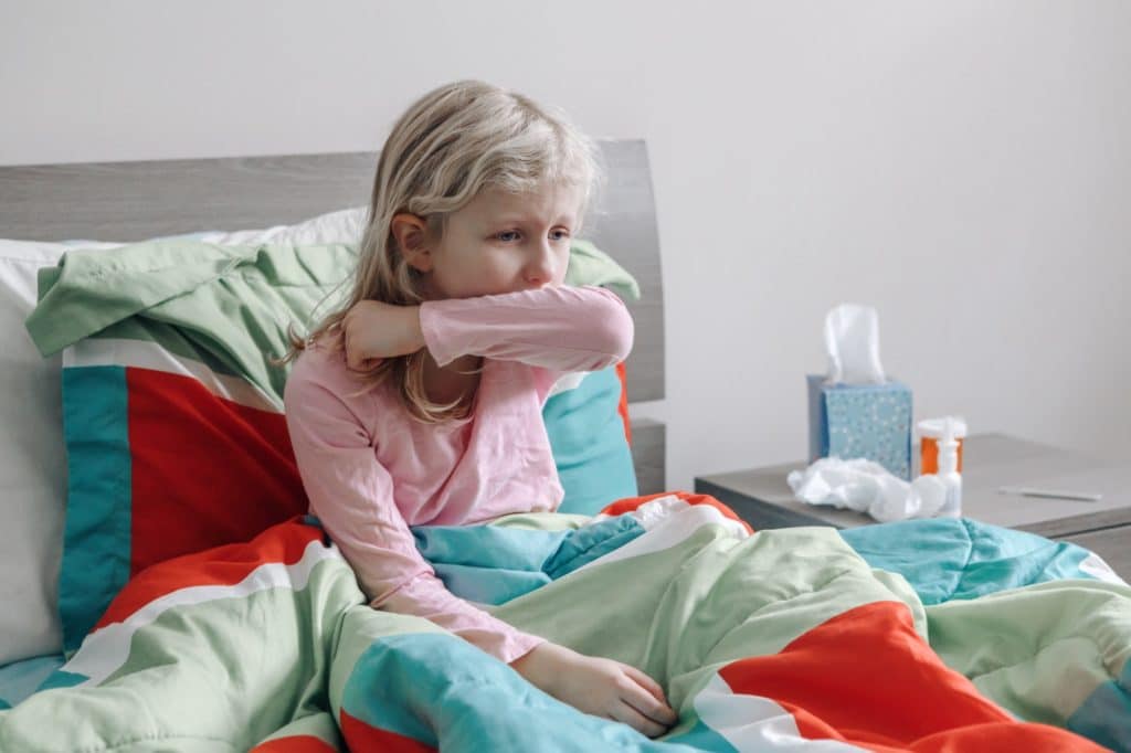 Sick ill Caucasian coughing girl with fever sitting in bed at home. Virus cold season illness