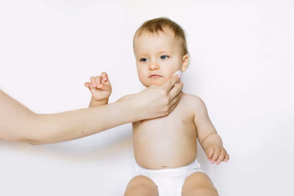 Young mom wiping the baby skin body and face with wet wipes carefully on white background. concept
